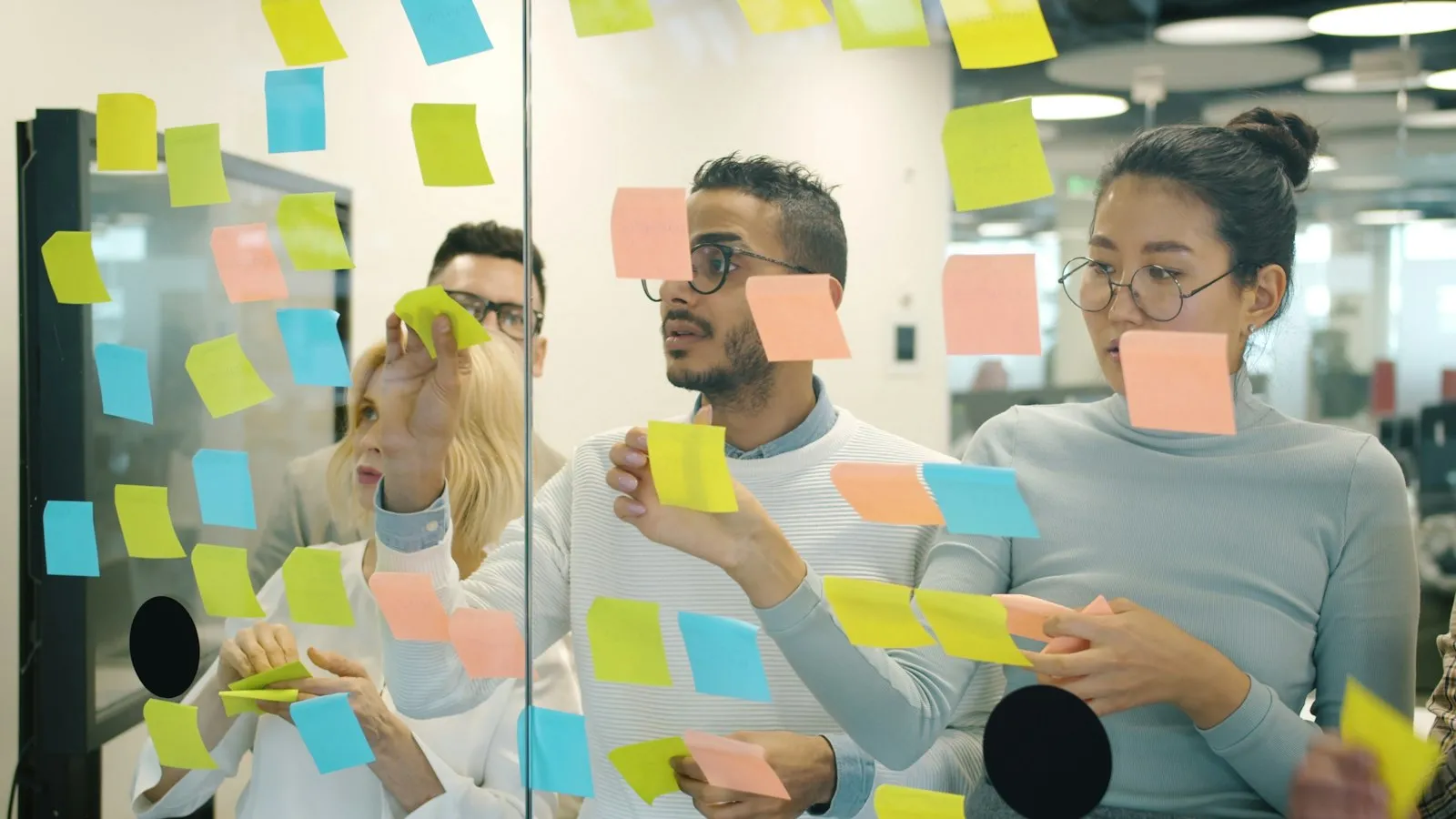 Colleghi che lavorano in gruppo con post-it colorati su una parete di vetro